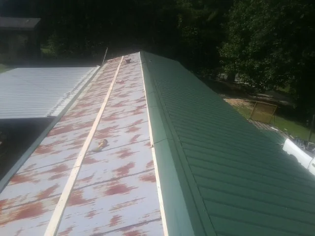 Old rusted panels beside newly installed green metal roofing — Wind Damage Roof Repair by Roofing Brothers in Pearisburg