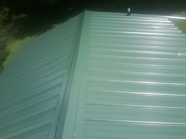 New green metal panels meeting at the ridge of a roof — Flat Roof Repair work by our crew in Pearisburg