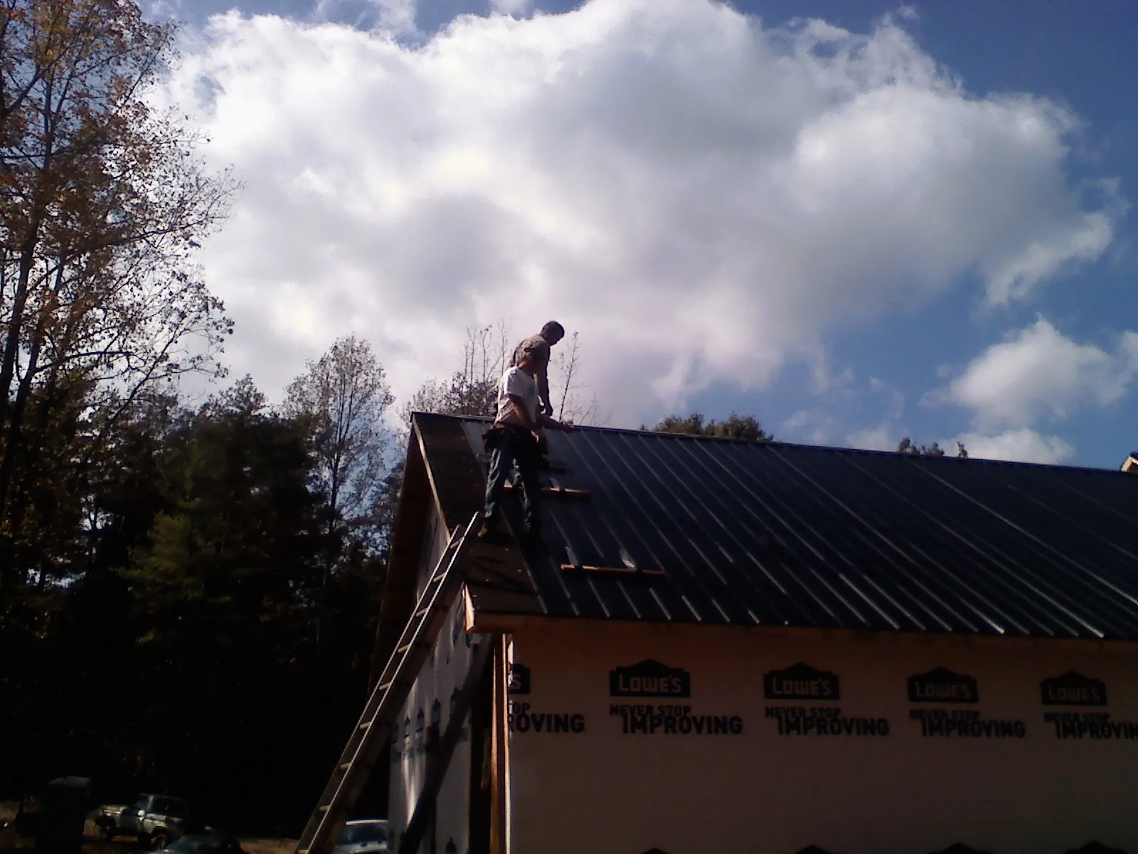 Roofer fastening dark metal panels high against a cloudy sky, from a Roof Inspection job in Pearisburg