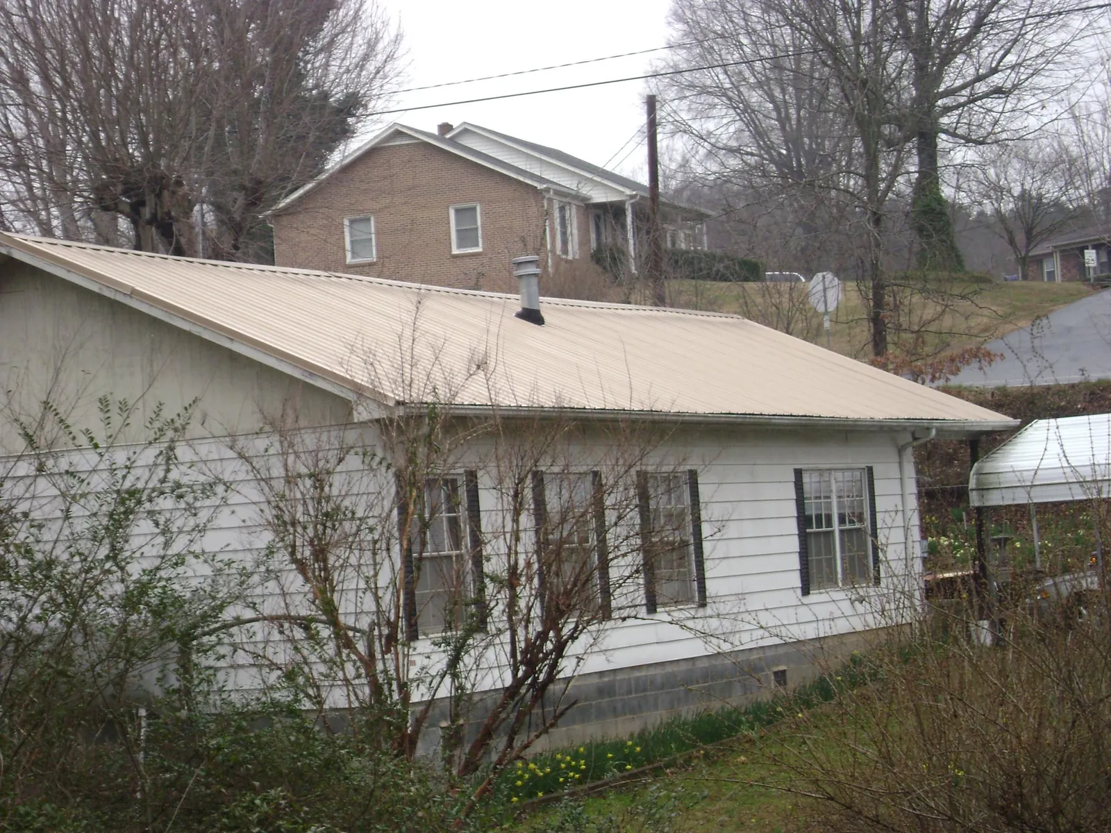 Tan metal roof on a white sided house set into a hillside — Commercial Roofing by Roofing Brothers in Pearisburg